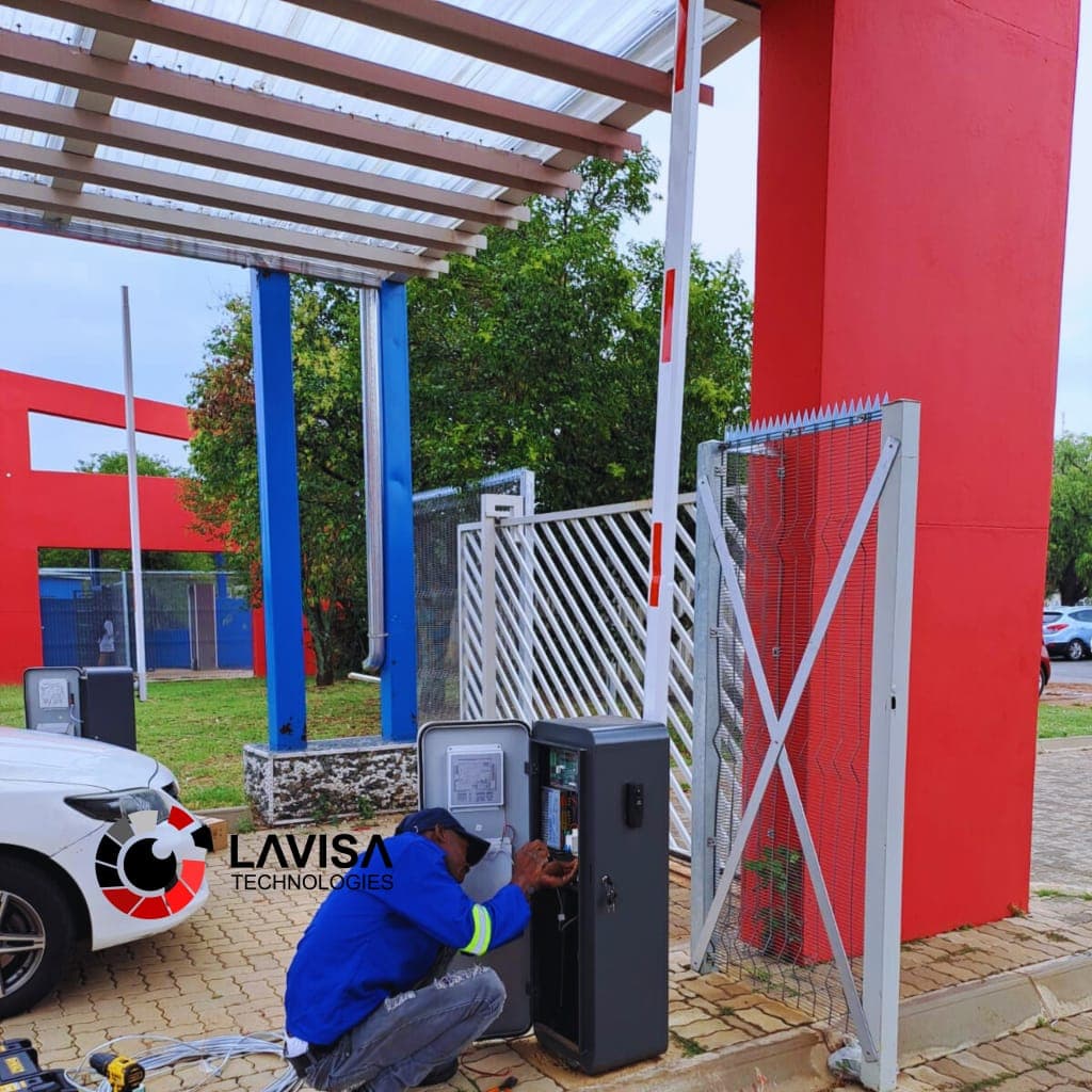 Technician in blue jacket repairs an open gate control box next to a red pillar.