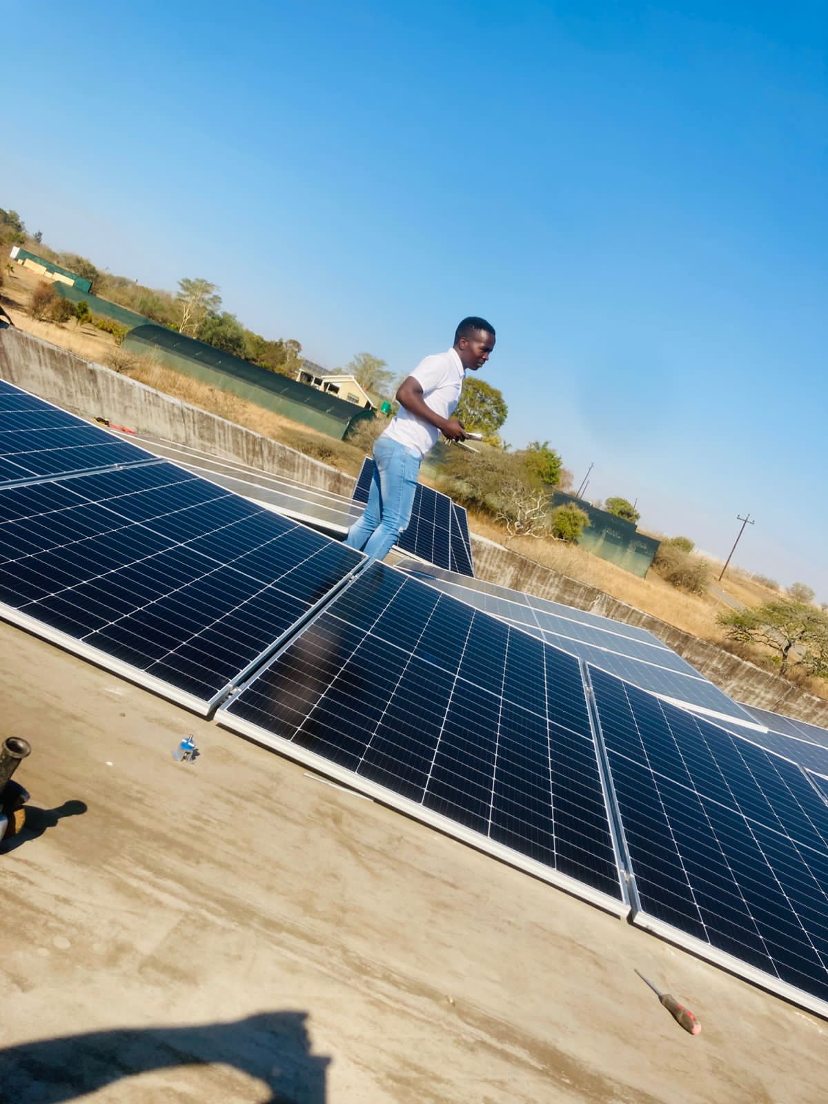 Technician in white shirt inspecting solar panels on a rooftop under a clear blue sky.